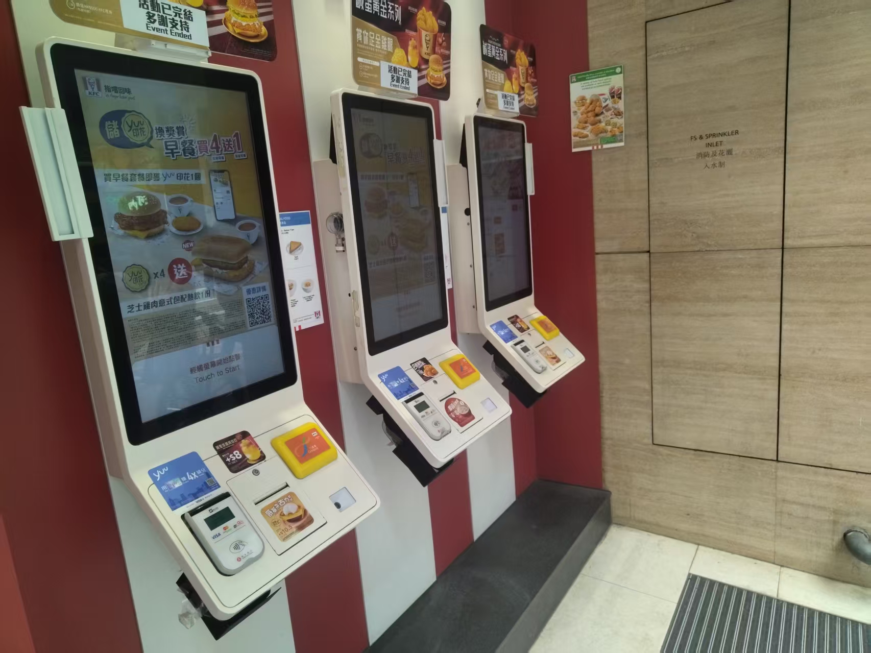 Three touchscreen self-checkout kiosks with payment panels in a restaurant