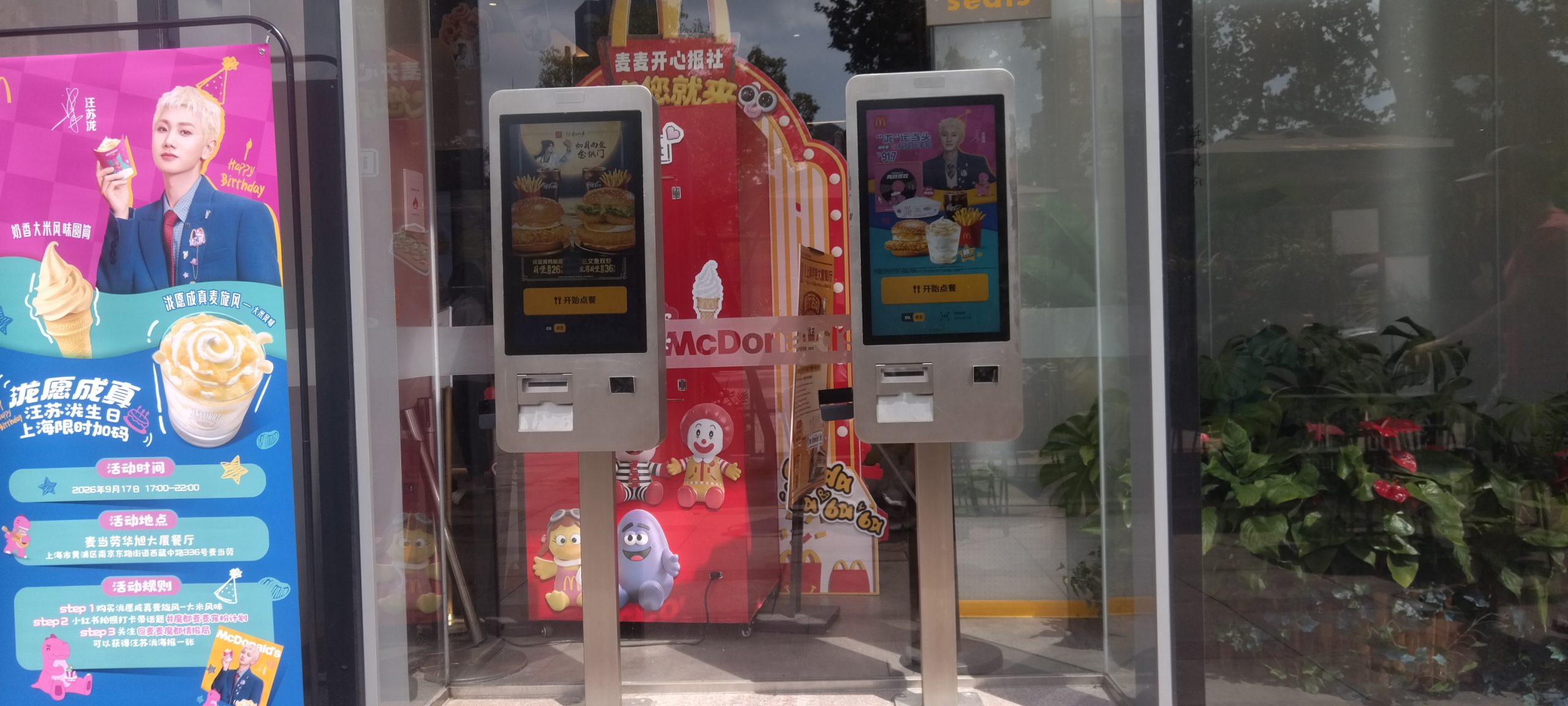 Two freestanding restaurant ordering kiosks displaying menu offers by the entrance