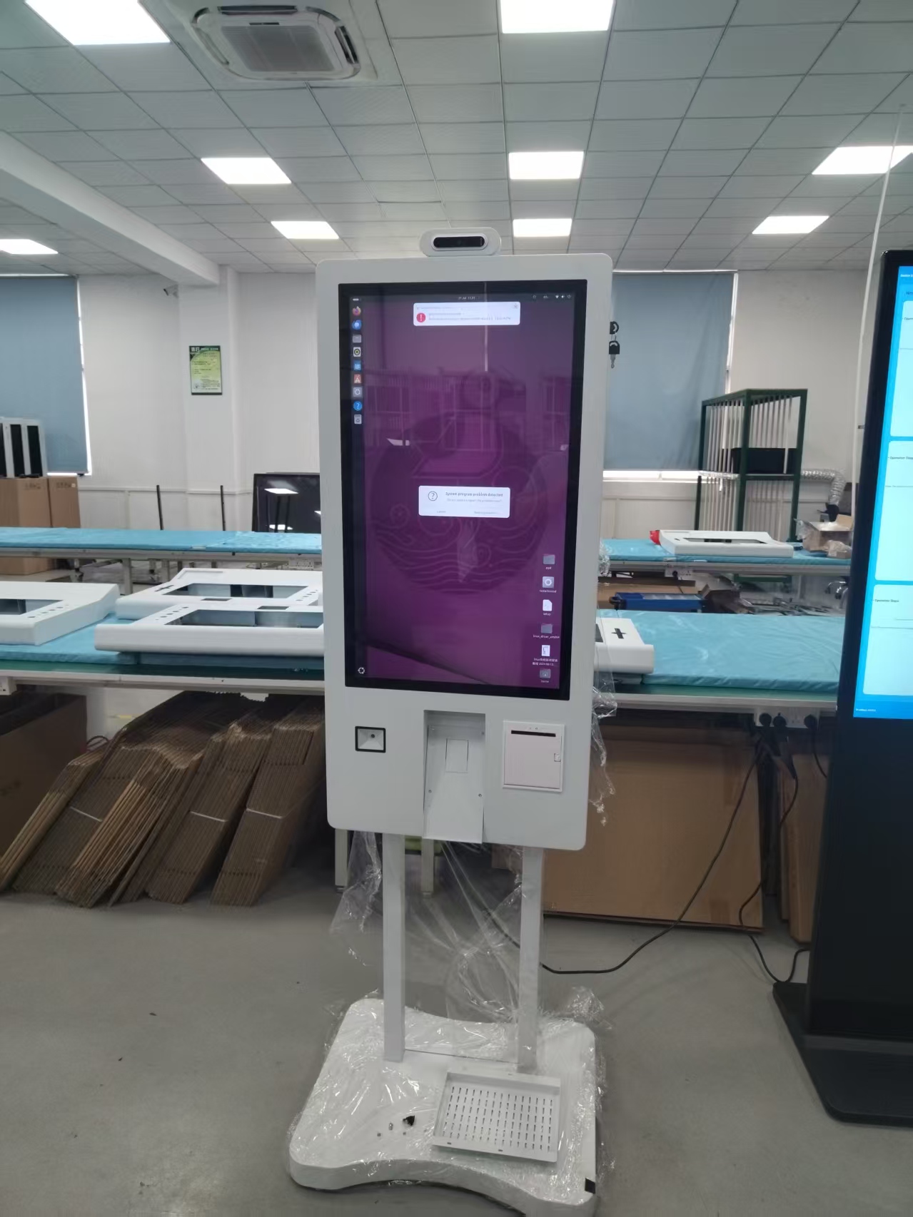 White self-ordering kiosk displaying a system message in an assembly workshop