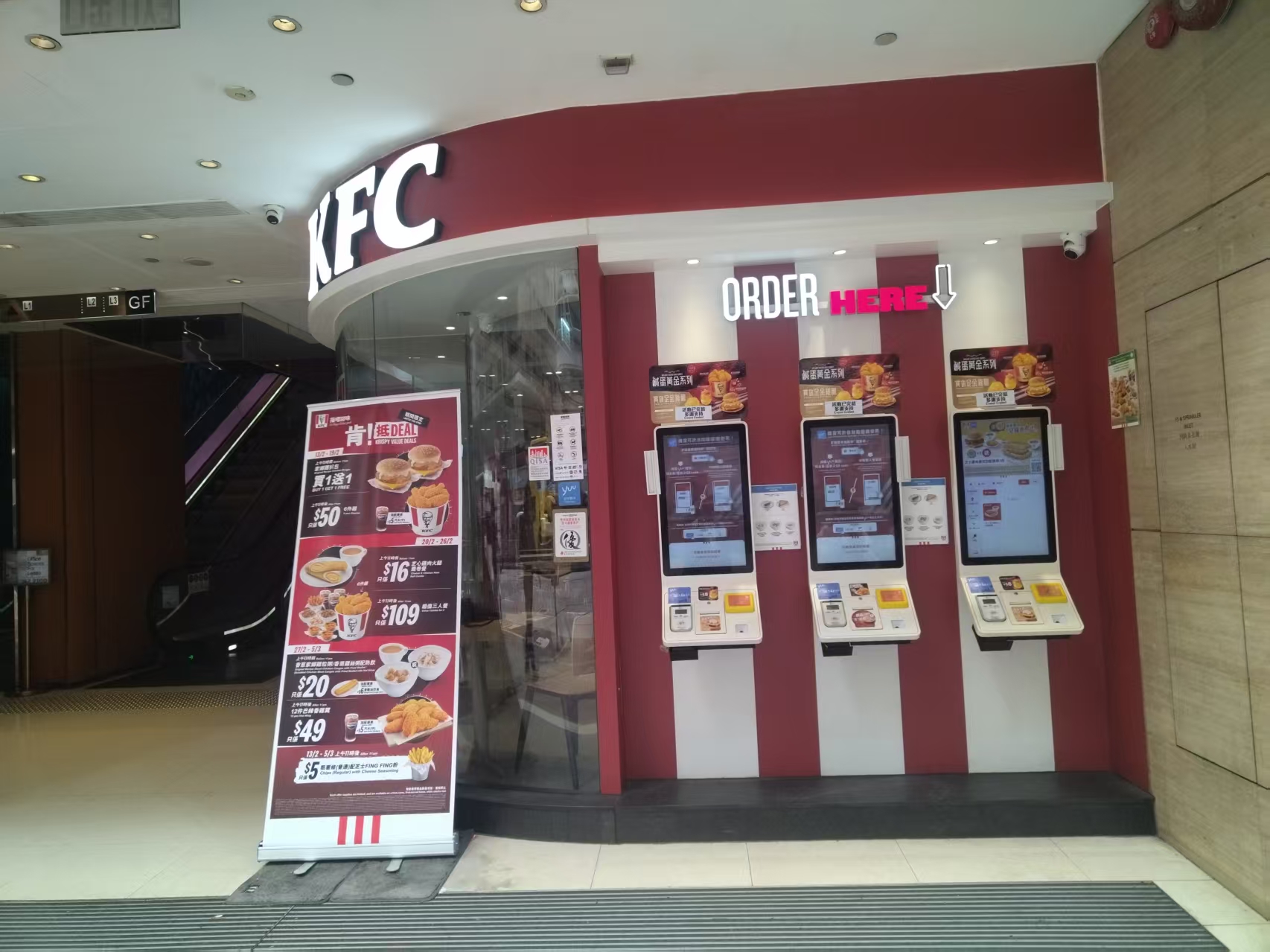 Self-checkout kiosks beside a restaurant entrance and menu display